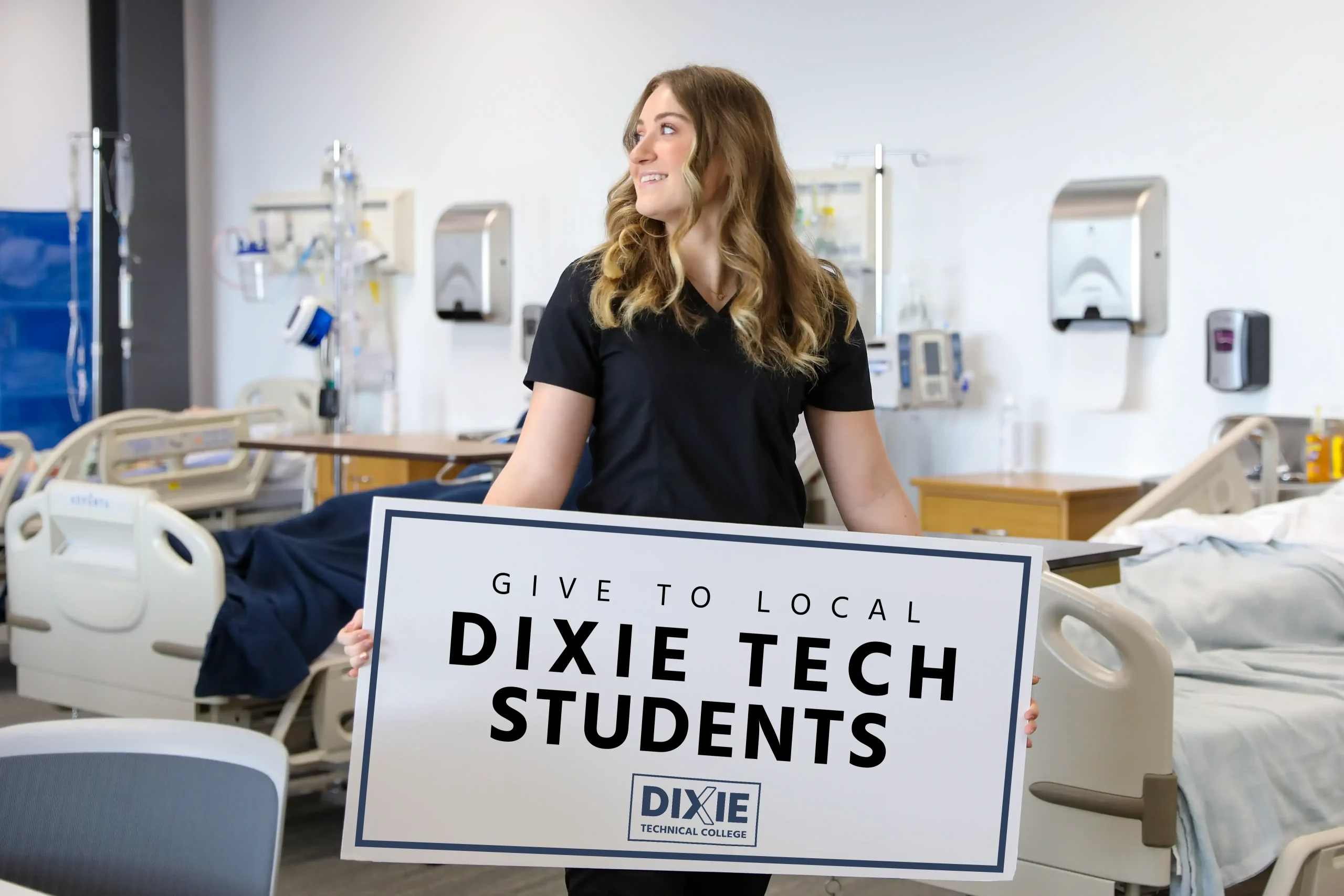 give to students in need A Dixie Tech Medical Technology Student holding a large sign that reads: Give to Local Dixie Tech Students!